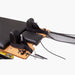 Set Pilates Home Metal Reformer machine close-up showing black padded headrests, black straps, wooden carriage, metal guide bars, and resistance cords on a light gray background.