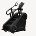 A black stair climber exercise machine with a digital display screen and curved handrails, shown from a three-quarters angle on a light gray background.