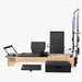 SET Pilates Master Wood Reformer with Tower with black padded mats and straps, shown on a plain light gray background. A separate black foot platform and a black storage box are placed in front of the machine.