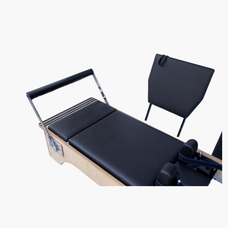 Pilates reformer machine with black padded straps and a light wood frame, shown on a plain light gray background.