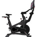 A black indoor stationary exercise bike with an attached angled digital display screen, shown against a solid white background.