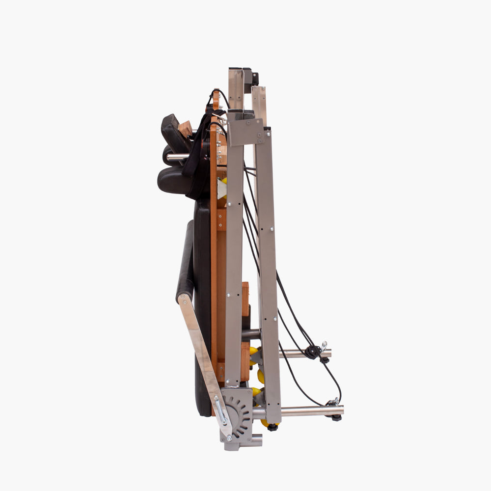 Set Pilates Folding Metal Reformer with a silver metal frame, black padded components, and brown side panels, shown on a plain light gray background.