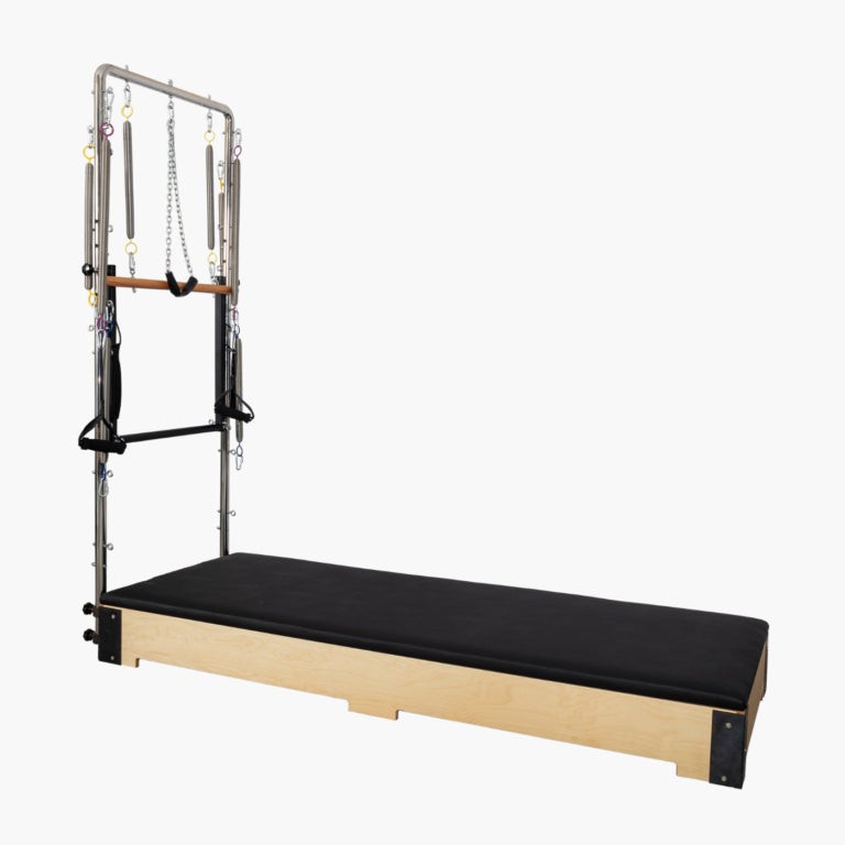 Set Pilates Tower Unit with a natural wood frame, black padded carriage, and metal tension apparatus on a plain light gray background.