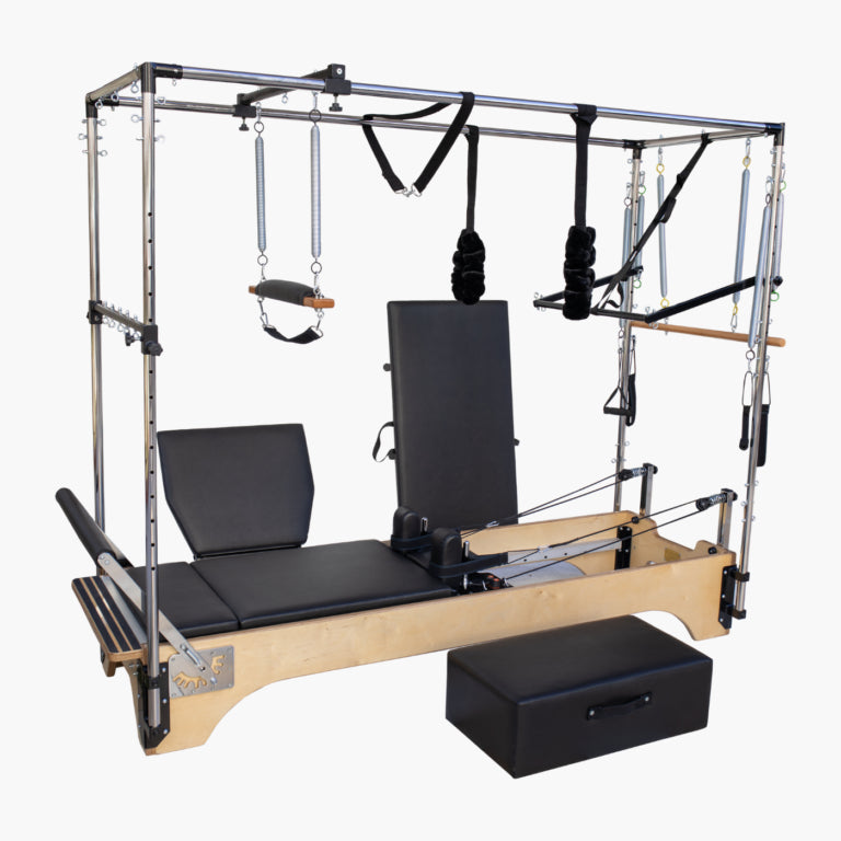 SET Pilates SECR Wooden Cadillac Reformer Trapeze Table with black padded bed and backrest, silver metal frame, hanging resistance bands and pulleys, wooden handlebar, and a separate black box on a plain light gray background.