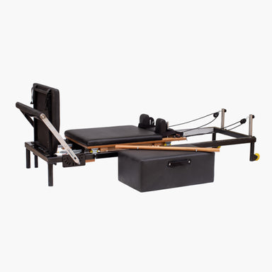 Set Pilates Home Metal Reformer with black padded mat and straps, wooden rails, metal frame components, and a black storage box on a light gray background.