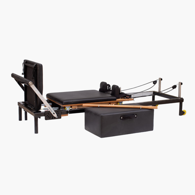 Set Pilates Home Metal Reformer with black padded mat and straps, wooden rails, metal frame components, and a black storage box on a light gray background.