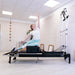 Woman exercising on a Pilates reformer machine in a studio setting.