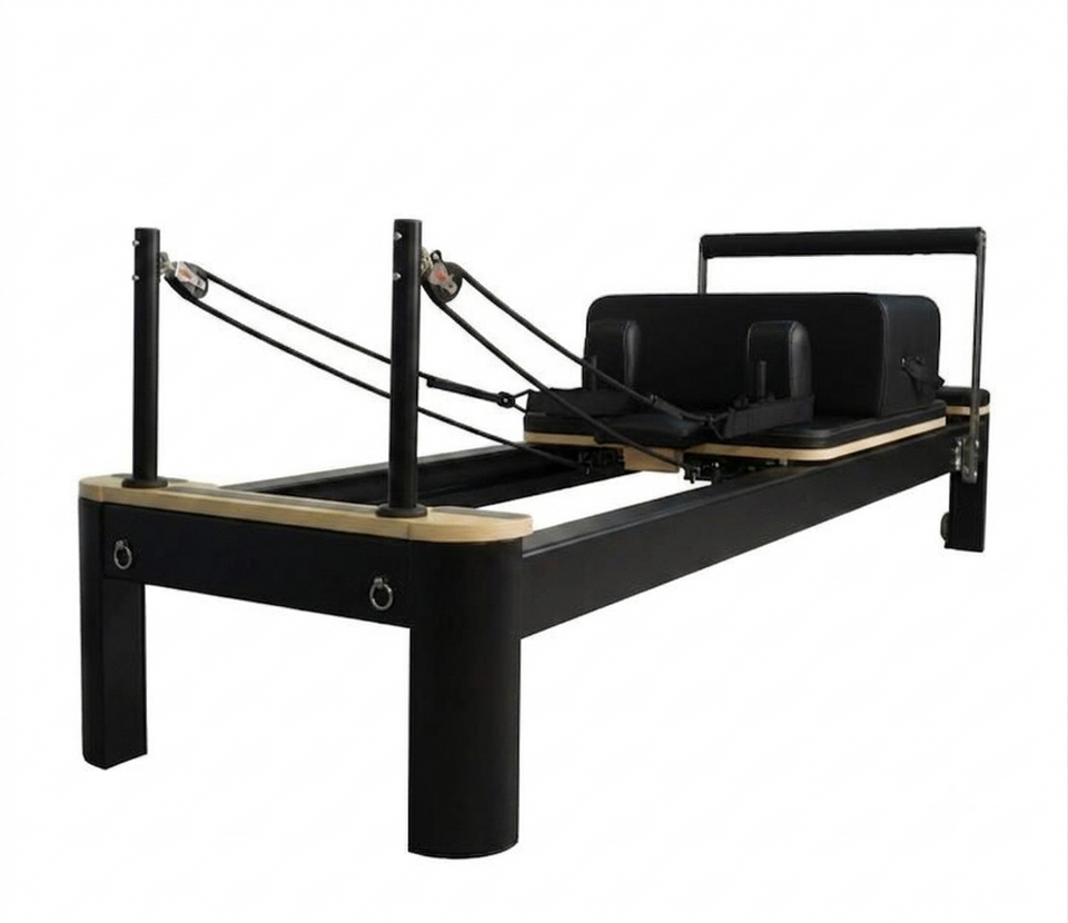 Origin Fitness Pilates reformer machine with a black frame, natural wood rails, and black straps, shown on a solid white background.