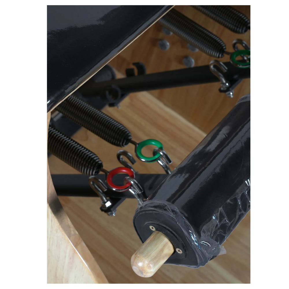 Close-up of a black wooden table leg assembly with metal springs, adjustment rings in red and green, and a light wood dowel on a light wood floor.