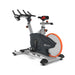 An indoor exercise bike with a dark gray and silver frame, a large gray flywheel with an orange rim, and black handlebars, shown on a white background.