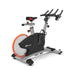 Origin Fitness Impulse PS450 Commercial Indoor Cycle with a black and silver frame, a large gray and orange flywheel, and black handlebars, shown on a white background.