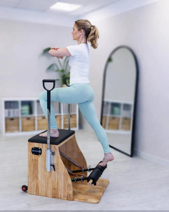 Woman exercising on a Pilates reformer machine in a home setting.