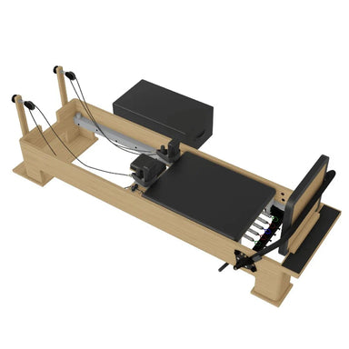 A wooden Pilates reformer machine with black padding, a black weight plate, and attached black straps, shown on a plain white background.