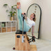 Woman exercising on a Pilates reformer machine in a home setting.