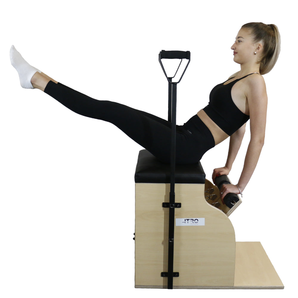 A woman performs a pilates exercise on a wooden reformer machine with a black handlebar, against a solid white background.