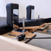 Pilates reformer machine close-up showing black padded handles, wooden frame, metal posts, and black resistance cords on a light wood platform.