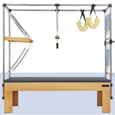 A Pilates reformer machine with a natural wood frame, black padded platform, metal tension rods, and hanging yellow resistance loops, shown against a plain white background.