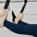 A close-up of a person's legs in navy blue leggings extended over a black suspension reformer machine with fluffy cream faux-fur cuffs.
