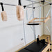 Pilates reformer machine with a wooden frame, black padded carriage, hanging straps, and fluffy cream grips in a bright indoor studio with white walls and wood floor.
