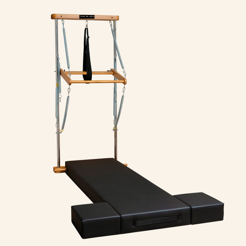 Atro Pilates Wall Tower Unit with Premium Mat with a black padded sliding track, two black foot blocks, and a wooden top bar suspended with straps and a hanging ring.