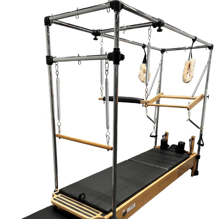 A Pilates reformer machine with a black padded mat, natural wood frame, and a metal canopy frame with hanging straps and wooden handles, shown on a plain white background.