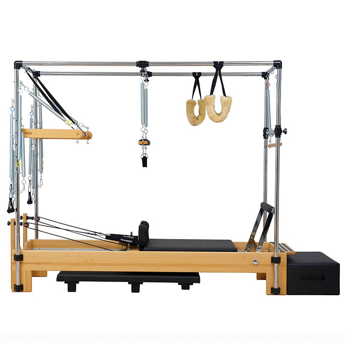 A Pilates reformer machine with a natural wood frame, black padded carriage, metal guide rails, spring-loaded resistance, hanging U-hand grips, and a black weight stack box, photographed on a plain white background.