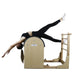 A woman performs a pilates exercise on a wooden reformer machine with a wooden ladder attachment, isolated on a white background.